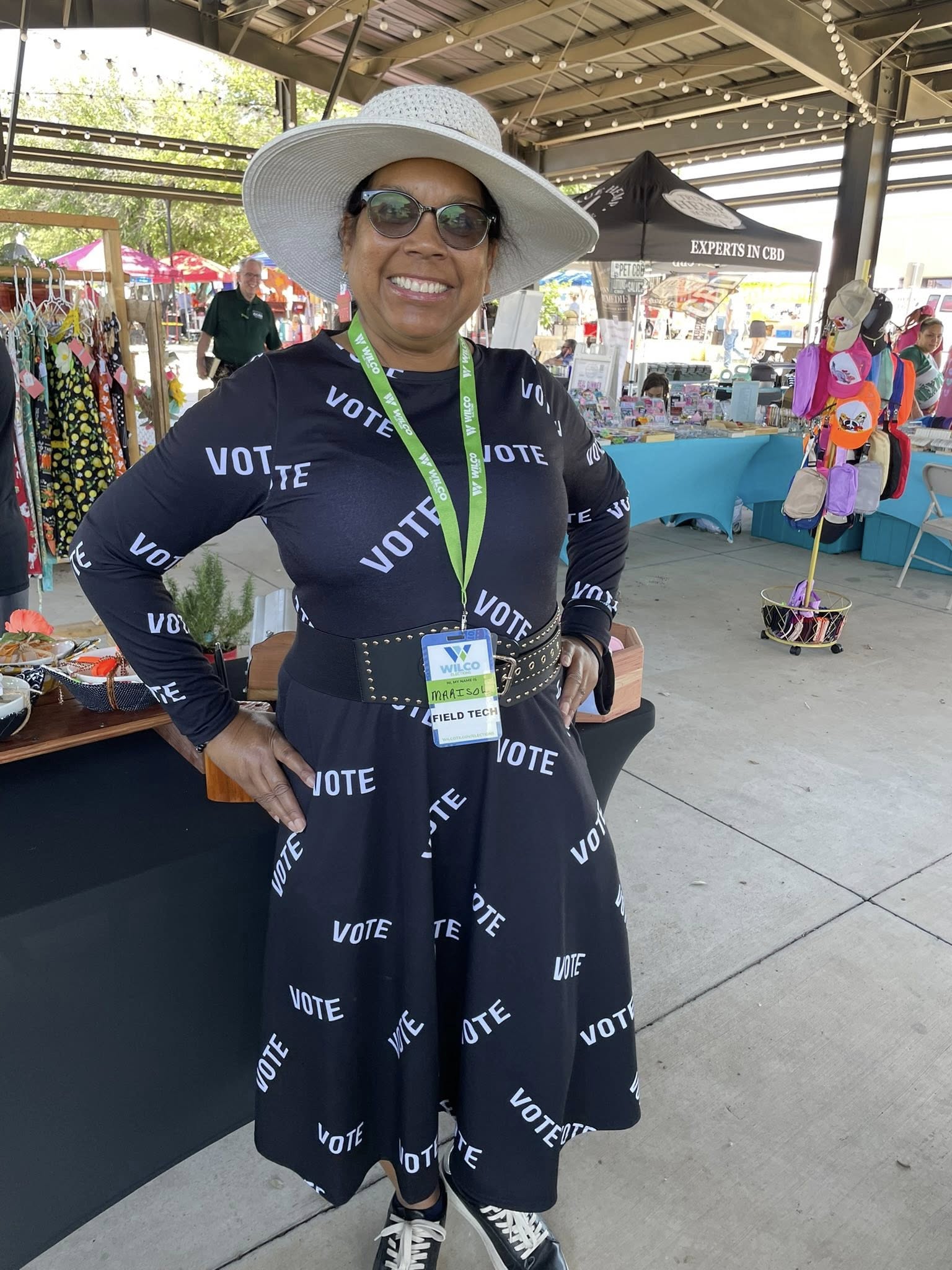 Marisol wears a big floppy white hat and a dark dress with white lettering reading VOTE scattered across it.