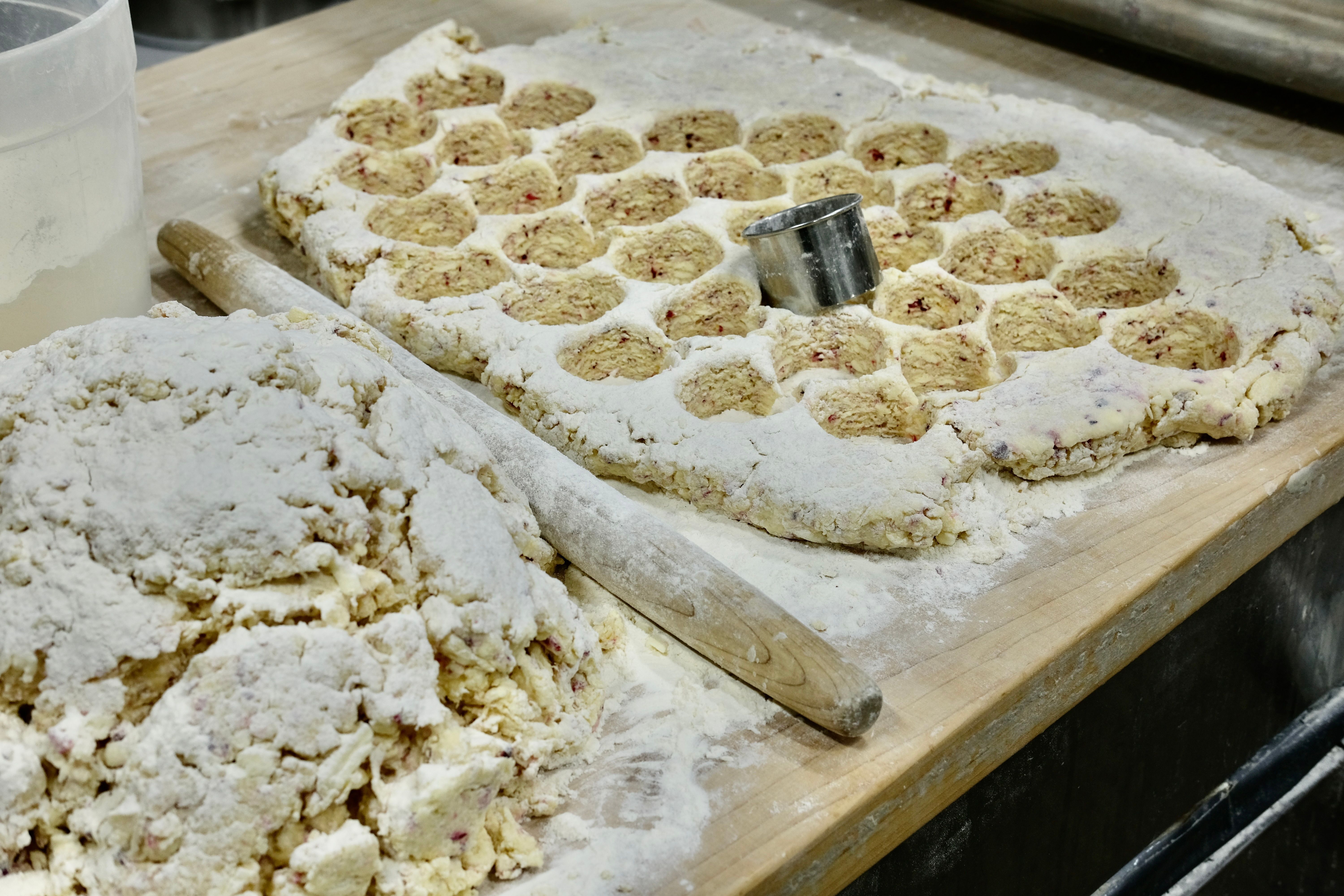 A mound of scone dough next to a rolled out sheet of scone dough with circles cut out, along with a wooden rolling pin and a silver circular cutter.