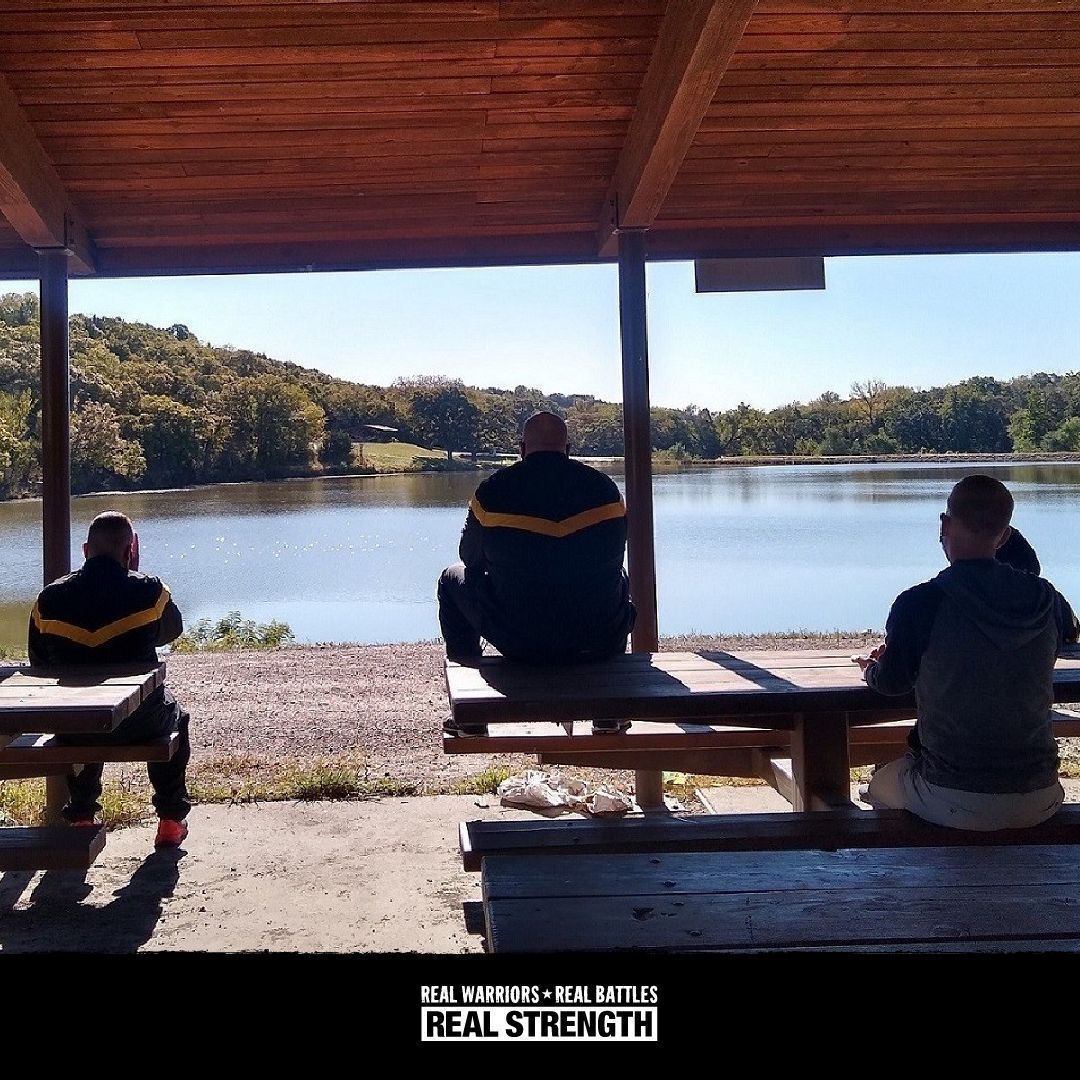 A photo of service members sitting on picnic tables outside with the Real Warriors logo at the bottom. 