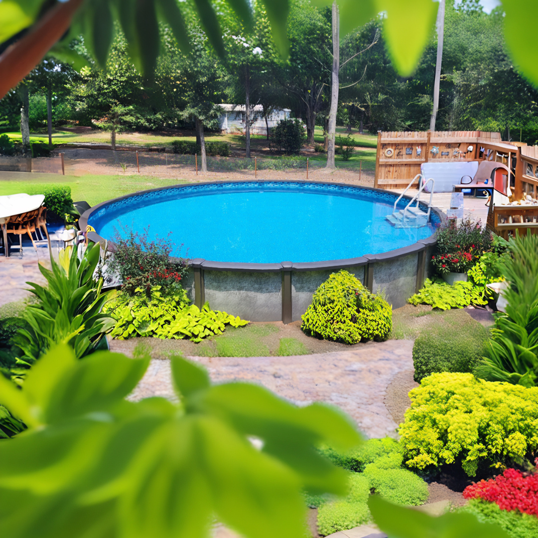 A landscaped backyard with an above ground swimming pool surrounded by greenery, colorful plants, a curved stone patio walkway, and a small wooden deck seating area on a sunny day